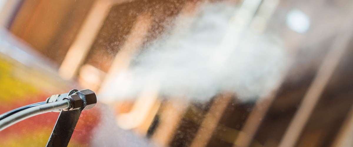AeroBarrier spray nozzle applying aerosolized sealant inside a framed building.